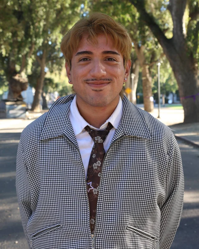 Jared smiling outdoors in a houndstooth jacket and floral tie, under a canopy of trees